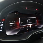 A car's interior at night with a view of the dashboard and a modern digital display, known as a cluster, that provides driving data and navigation