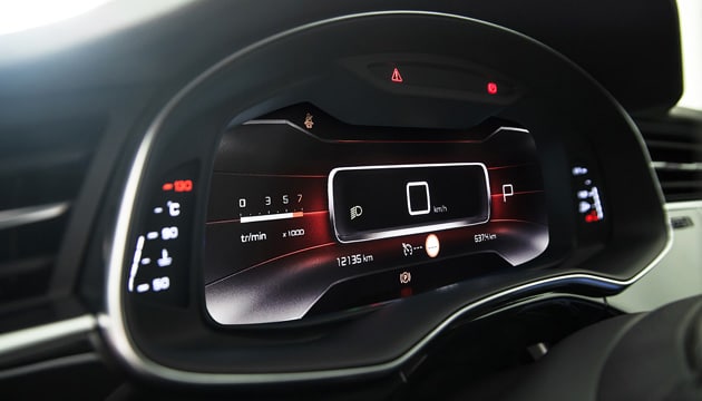 A car's interior at night with a view of the dashboard and a modern digital display, known as a cluster, that provides driving data and navigation