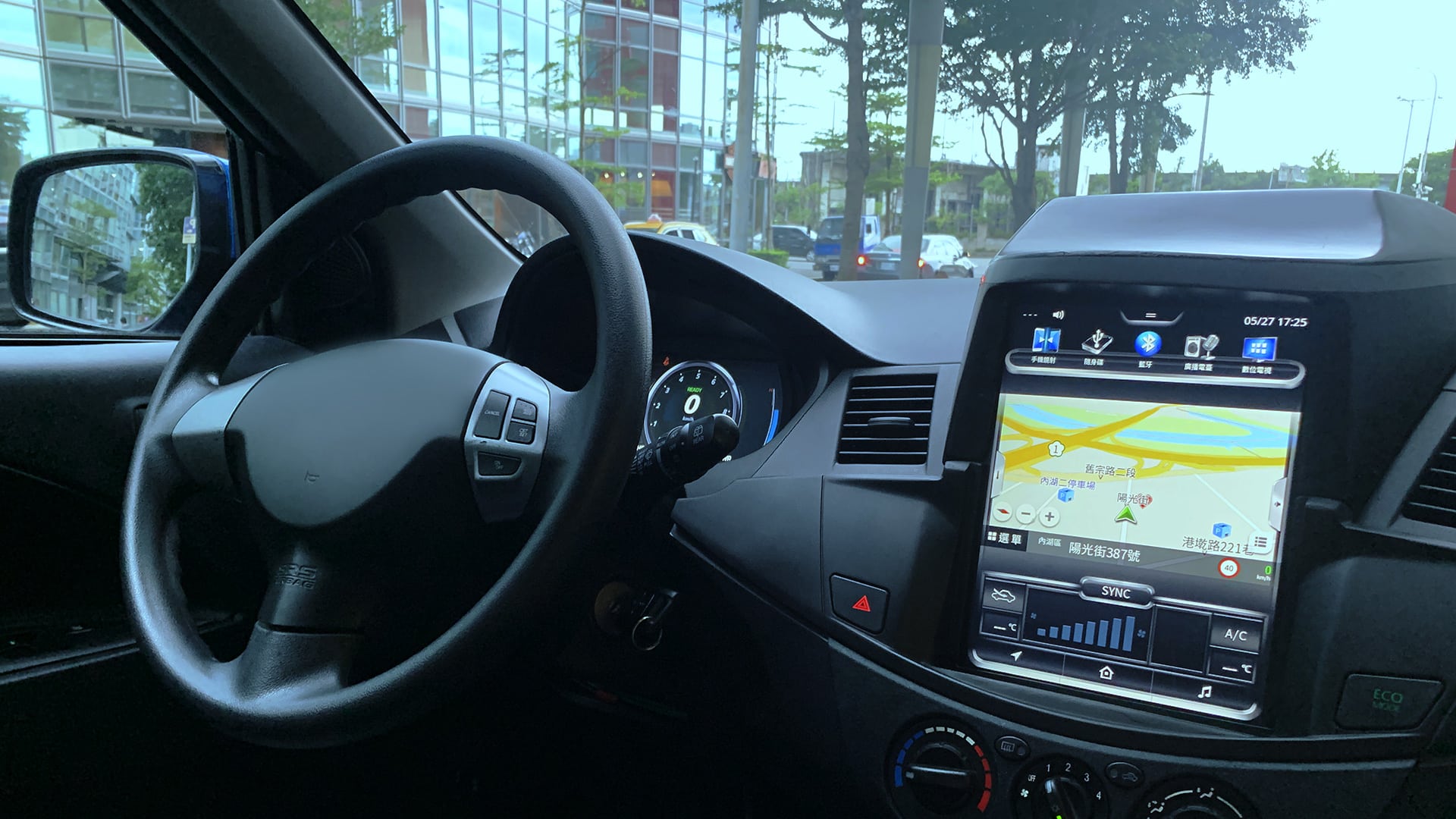 A car's dashboard with an in-vehicle infotainment (IVI) system displaying a navigation map, set against a city street view through the windshield.
