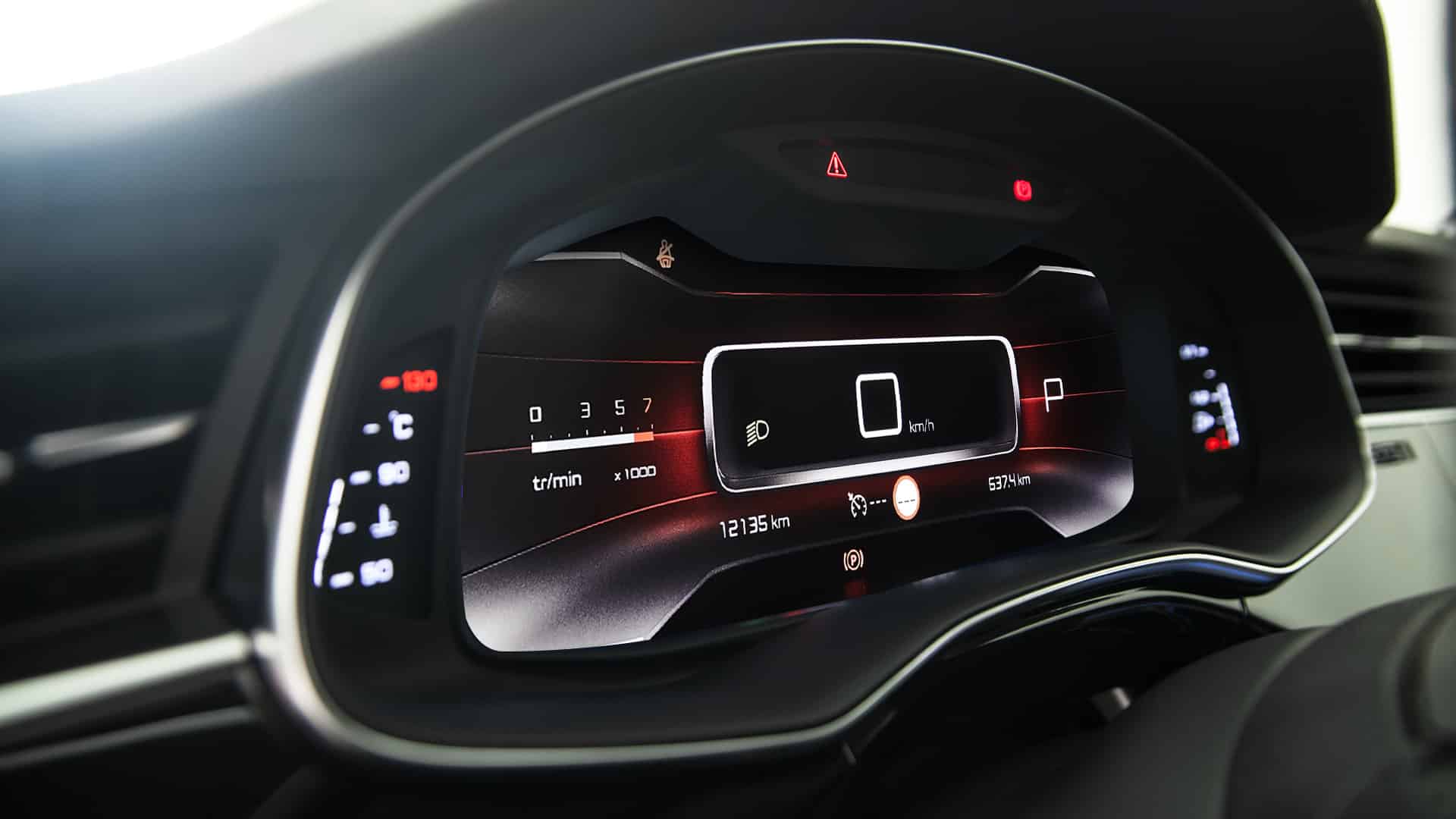 A car's interior at night with a view of the dashboard and a modern digital display, known as a cluster, that provides driving data and navigation